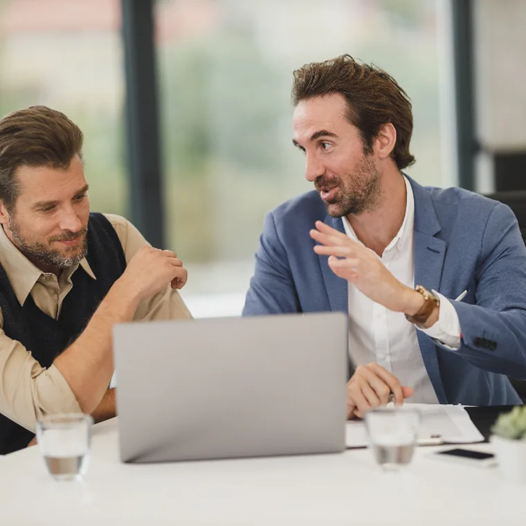 Two colleagues talking over an open laptop at a meeting table
