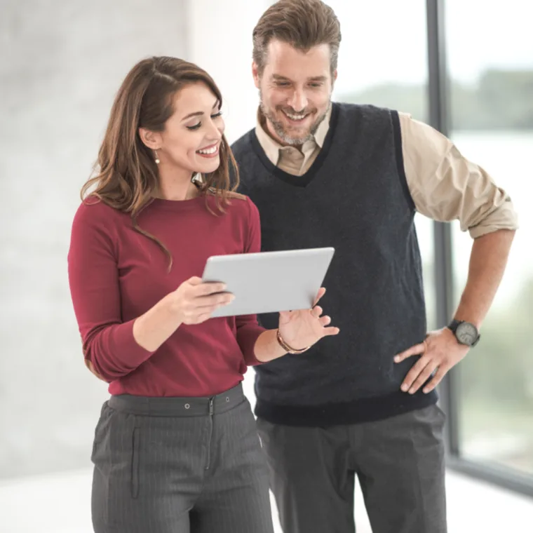 Two colleagues standing in a bright office, reviewing work together on a tablet