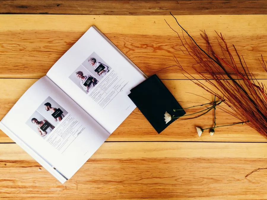 An open printed brochure lying on a wooden surface beside a notebook